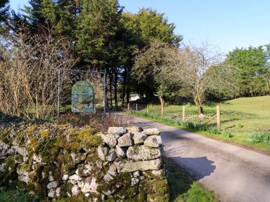 A country road entrance with a moss-covered stone wall and a sign reading old waterslack farm surrounded by trees and fenced grassy area at Lodge 4 in Silverdale