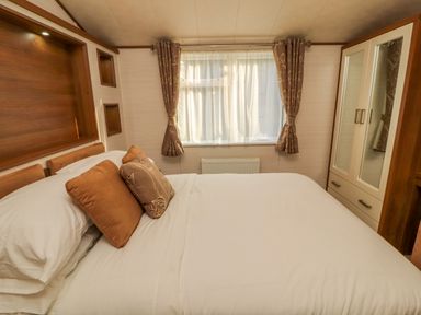 A bedroom with a bed with pillows beside a window with curtains and a wardrobe at Lodge 4 Silverdale