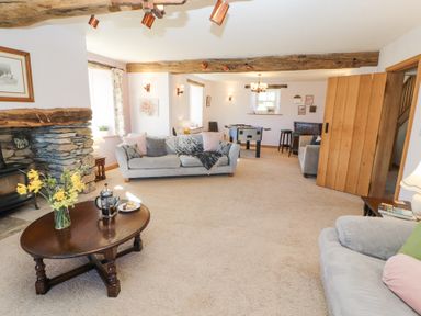 A living room with sofas a wooden coffee table flowers a stone fireplace and a foosball table at High Wood Foot in Bampton Cumbria