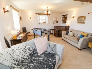 A room with two sofas a foosball table a wooden bar two bar stools and a sideboard with a lamp at High Wood Foot in Bampton Cumbria
