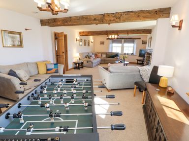 A living room with sofas a foosball table wooden beams and a lamp on a sideboard at High Wood Foot in Bampton Cumbria