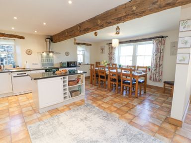 A kitchen and dining area with wooden beams a dining table with chairs and kitchen island at High Wood Foot in Bampton Cumbria