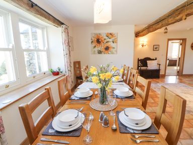 A dining room with a wooden table set with plates bowls glasses and a vase of yellow flowers at High Wood Foot in Bampton Cumbria