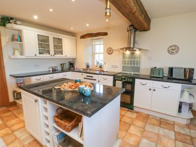 A kitchen with white cabinets a black countertop an island with pastries and cups a green oven a toaster and a microwave at High Wood Foot in Bampton Cumbria