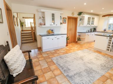 A kitchen with white cabinets a wooden bench with a white cushion tiled floor and a rug at High Wood Foot in Bampton Cumbria