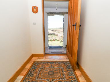 A hallway with a patterned rug on the floor and an open wooden door leading outside at High Wood Foot in Bampton Cumbria