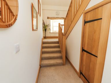 A hallway with carpeted stairs wooden banister a wooden door and a window with a plant at High Wood Foot in Bampton Cumbria