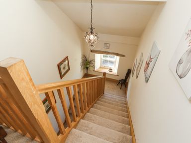 A carpeted staircase with wooden railing leading down to a window seat with a chair near the window at High Wood Foot in Bampton Cumbria