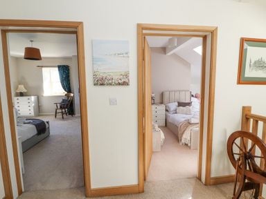 Two bedrooms visible through open doors with beds dressers and chairs in a hallway at High Wood Foot in Bampton Cumbria