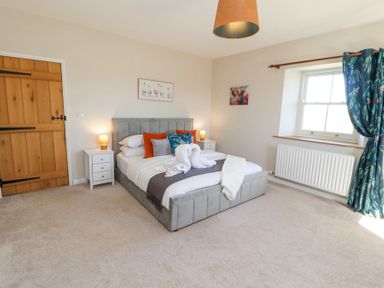 A bedroom with a double bed two bedside tables with lamps a wooden door and a window with blue curtains at High Wood Foot in Bampton Cumbria