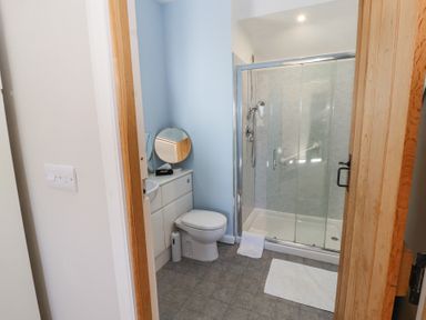 A bathroom with a toilet a shower cubicle and a counter with a round mirror at High Wood Foot in Bampton Cumbria