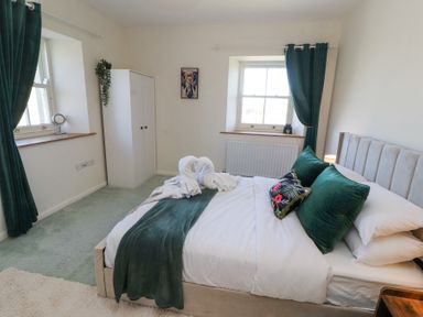 A bedroom with a bed with green pillows and blanket two windows with green curtains a white wardrobe and a wall painting at High Wood Foot in Bampton Cumbria