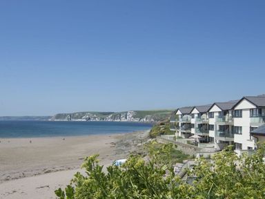 A beach with sand and sea next to cliffside buildings at 6 Burgh Island in Bigbury-On-Sea