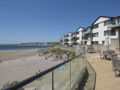 A beachside view with sand and ocean next to a patio with tables and chairs at 6 Burgh Island in Bigbury-On-Sea