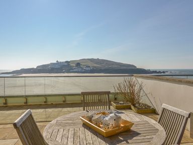 A wooden outdoor table with a tea set and chairs on a patio overlooking a beach and an island at 6 Burgh Island in Bigbury-On-Sea