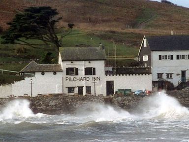 A building labeled Pilchard Inn near a rocky shore with waves crashing at 6 Burgh Island in Bigbury-On-Sea
