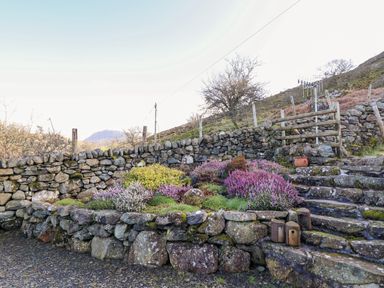 A stone wall with colorful bushes and stone steps leading uphill at Tyn Y Graig in Fairbourne