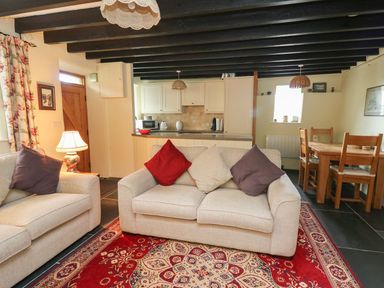 A living room with beige sofas and cushions next to a dining table and kitchen at Tyn Y Graig in Fairbourne