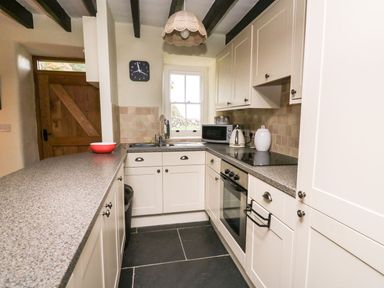 A kitchen with white cabinets a countertop microwave kettle and oven at Tyn Y Graig in Fairbourne