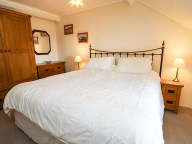 A bedroom with a large bed with white bedding wooden wardrobe wooden dresser and two bedside tables with lamps at Tyn Y Graig in Fairbourne