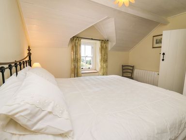 A bedroom with a bed a window with curtains a chair and a wardrobe at Tyn Y Graig in Fairbourne