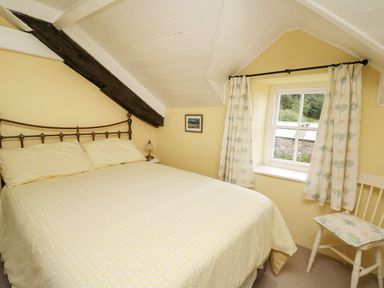A bedroom with a double bed yellow bedding a window with floral curtains and a chair at Tyn Y Graig in Fairbourne