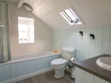 A bathroom with a bathtub a toilet a sink and two fish-shaped hooks on the wall at Tyn Y Graig in Fairbourne
