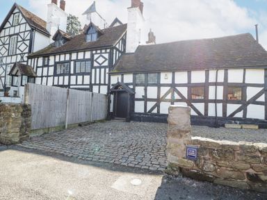 A cobblestone driveway and timber framed buildings with white and black walls at Wyre Court Cottage in Bewdley