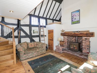 A living room with patterned sofas wooden stairs a brick fireplace and a framed poster at Wyre Court Cottage in Bewdley