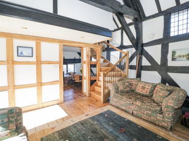 A living room with patterned sofas a wooden staircase and exposed wooden beams at Wyre Court Cottage in Bewdley