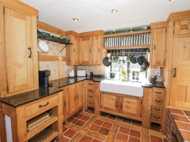 A kitchen with wooden cabinets a white sink hanging pans and cooking utensils at Wyre Court Cottage in Bewdley