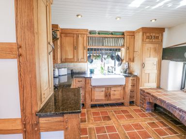 A kitchen with wooden cabinets a white sink hanging pots and pans and tiled floor at Wyre Court Cottage in Bewdley