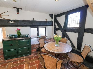 A kitchen area with a green stove a round tiled table with a vase of flowers and four wicker chairs at Wyre Court Cottage in Bewdley