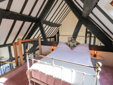 A bedroom with a white metal bed frame and floral pillow in an attic with exposed dark wooden beams at Wyre Court Cottage in Bewdley