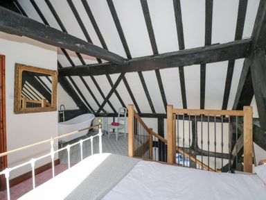 A bedroom with a white bed frame a bathtub a chair a mirror and black ceiling beams at Wyre Court Cottage in Bewdley