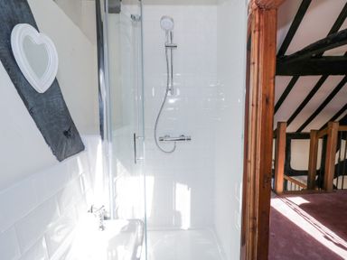 A shower with white tiles a heart shaped mirror and a wooden doorway leading to a stairway at Wyre Court Cottage in Bewdley