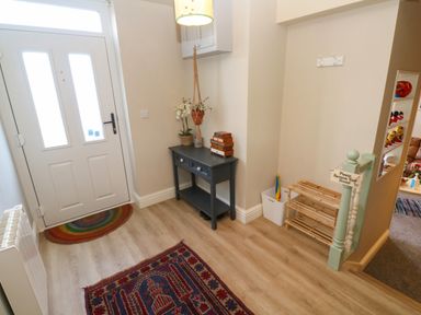 An entryway with a white door a dark small table with drawers a plant a shoe rack and a sign asking to remove shoes at Cottage Annex in Constantine