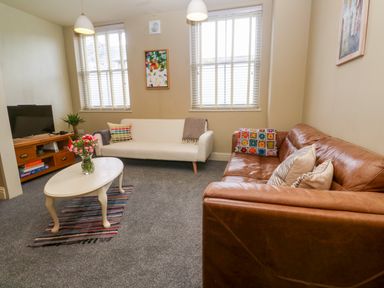 A living room with two sofas a coffee table with flowers and a television on a wooden stand at Cottage Annex in Constantine