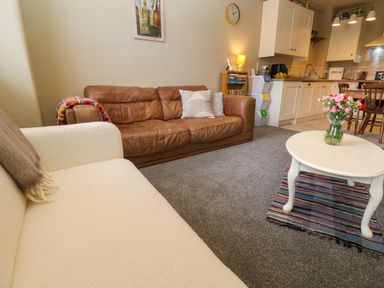 A living room with a brown leather sofa and a white sofa a coffee table with flowers and kitchen in the background at Cottage Annex in Constantine