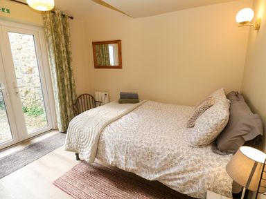 A bedroom with a bed a chair a mirror and glass doors with green curtains at Cottage Annex in Constantine