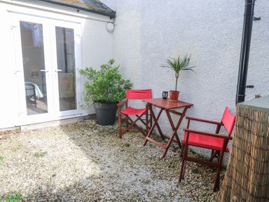 A small patio with a wooden table and two red chairs with potted plants near white doors at Cottage Annex in Constantine