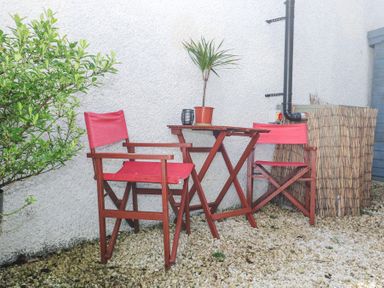 A small outdoor seating area with two red chairs and a wooden table with a potted plant and a small lantern on it at Cottage Annex in Constantine