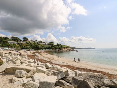 A beach with large rocks in the foreground people walking on the sand houses and greenery on a hill in the background at Cottage Annex in Constantine