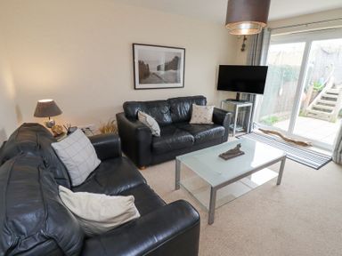A living room with two black leather sofas a glass coffee table a lamp and a television by a sliding glass door at Sea Shore in Seahouses