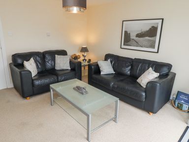 A living room with two black leather sofas a glass coffee table and a framed photo on the wall at Sea Shore in Seahouses