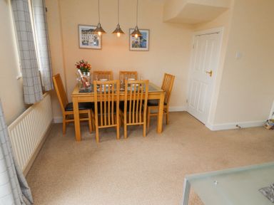A dining area with a wooden table and six chairs under three hanging lights at Sea Shore in Seahouses