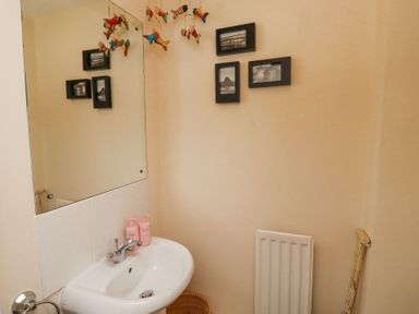 A bathroom sink with two pink bottles on it a large mirror above the sink three black framed pictures on the wall a radiator and a wooden object in the corner at Sea Shore in Seahouses