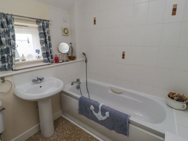 A bathroom with a sink a bathtub a window with curtains and decorative items at Sea Shore in Seahouses
