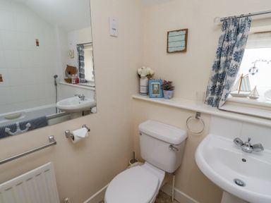 A bathroom with a toilet sink mirror and window with curtain at Sea Shore in Seahouses