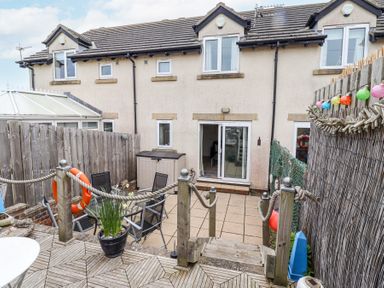 A backyard patio with wooden deck steps leading down to a tiled area with outdoor chairs and a storage box at Sea Shore in Seahouses